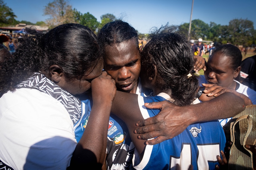 Three young people wearing blue hug on a football field