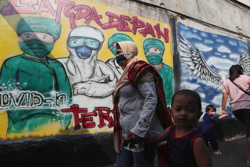 A woman wearing a mask walks with her child in an Indonesian neighbourhood.