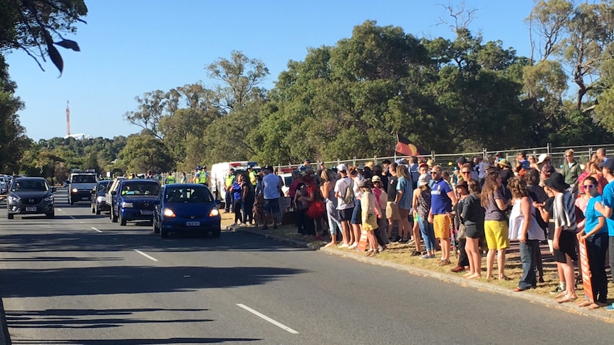 Dozens of people on the side of a road with poliice present