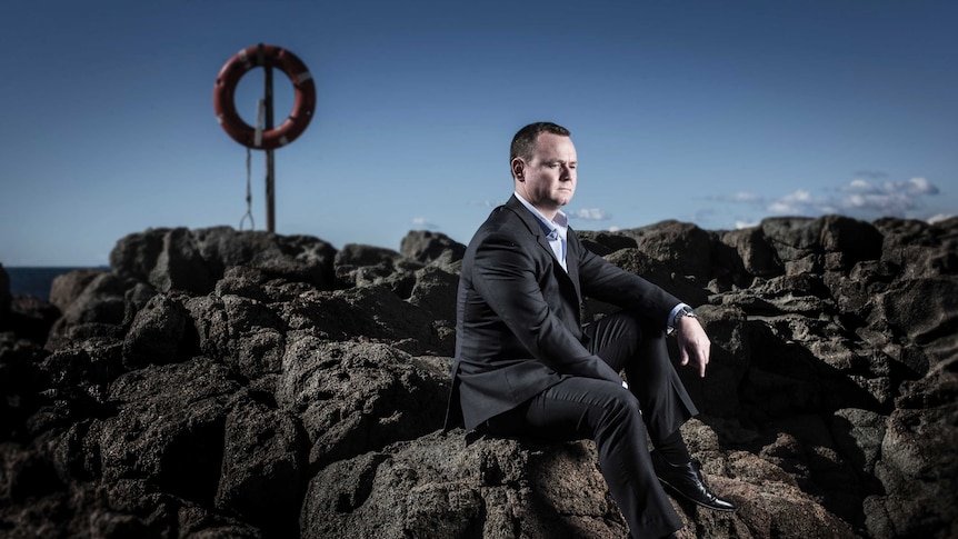 Michael Bainbridge sits on some rocks looking off camera.