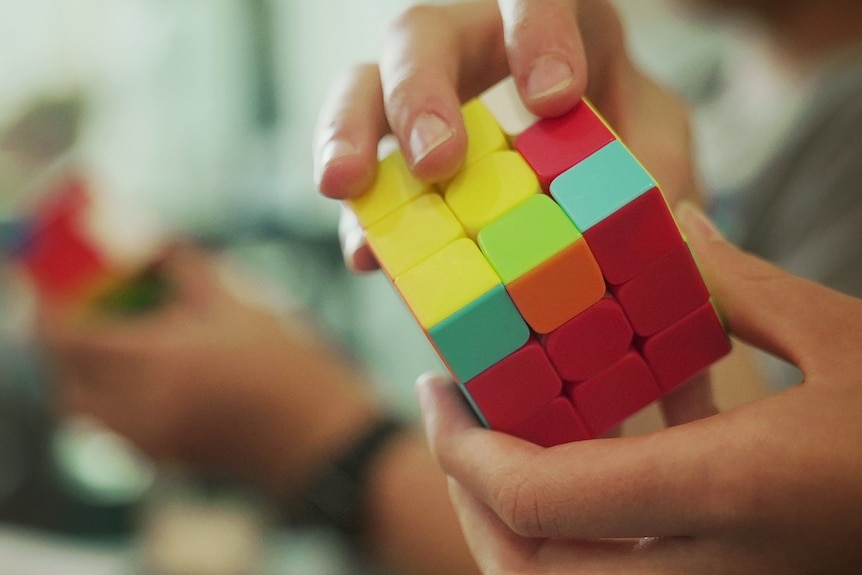 A close up of some hands on a Rubik's cube.