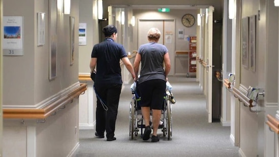 Aged care workers accompany a resident down the hallway of their facility