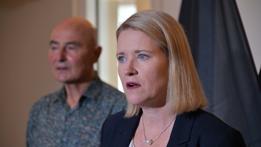 Acting NT Chief Minister Nicole Manison is standing in front of a camera and talking. She looks serious, Hugh Heggie is behind.