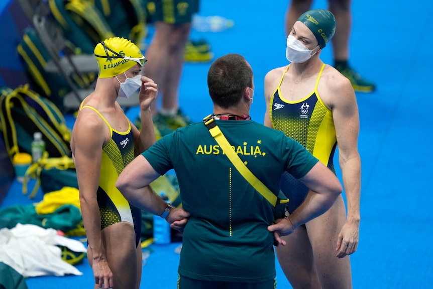 Two Australian swimmers talk to a swimming coach the the Olympic pool in Tokyo.