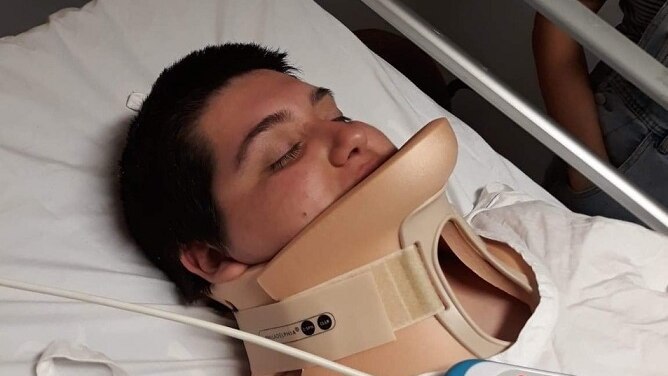 A young woman with short hair lies on what looks like a hospital bed, in a neck brace.