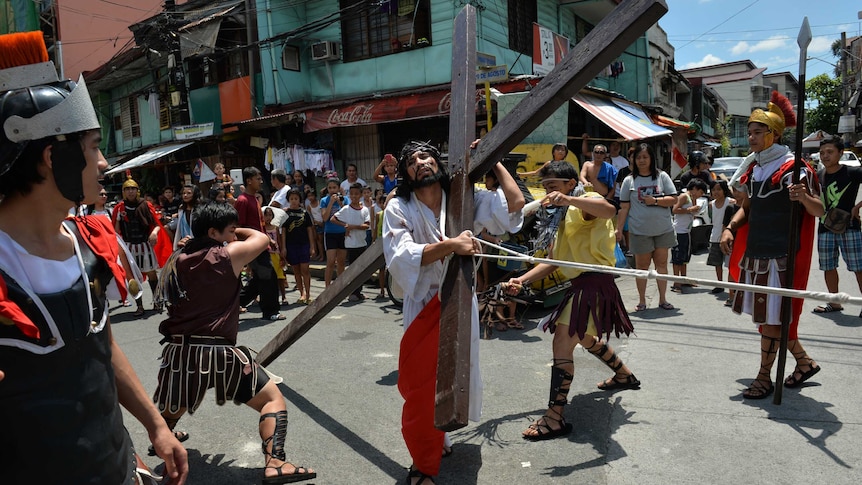 A man acting as Jesus carries a wooden cross