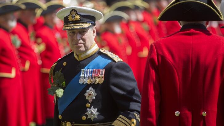 Prince Andrew looks to the right as he stands among a sea of Chelsea Pensioners. He wears black military garb.