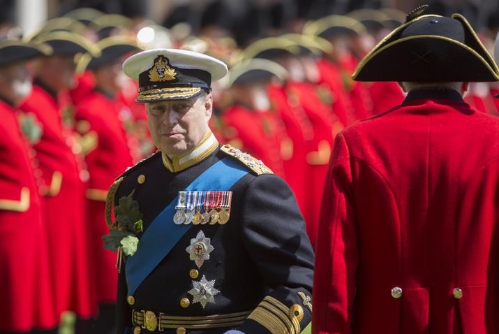 Prince Andrew looks to the right as he stands among a sea of Chelsea Pensioners. He wears black military garb.