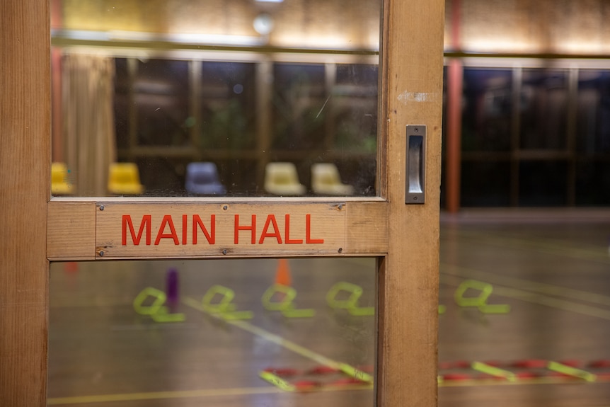 A door with the words 'main hall' in the foreground, in the background, exercise equipment is set up.