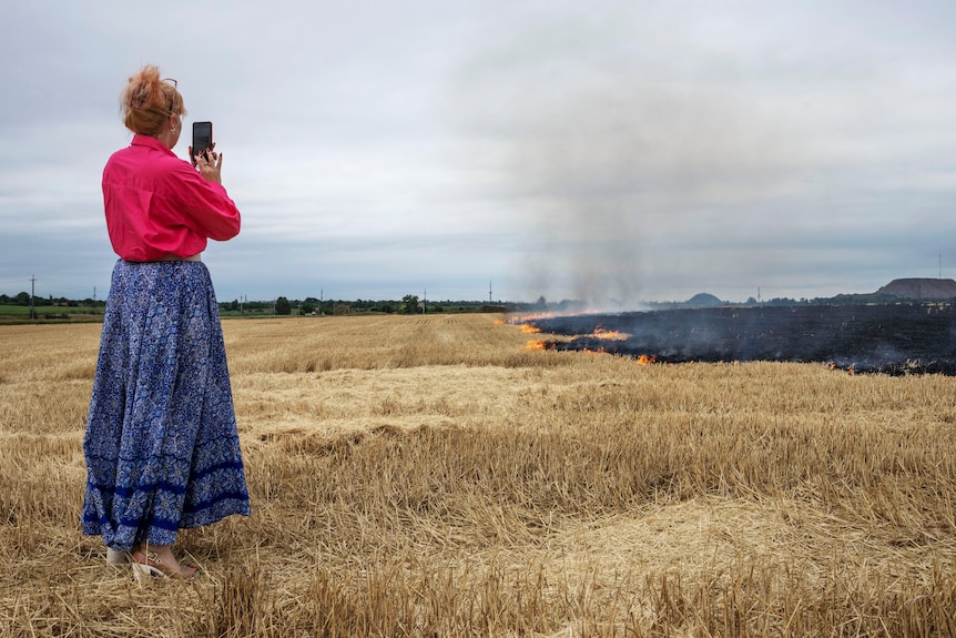 Medic volunteer Nataliia Voronkova stands in a field with her phone out filming a grass fire. 