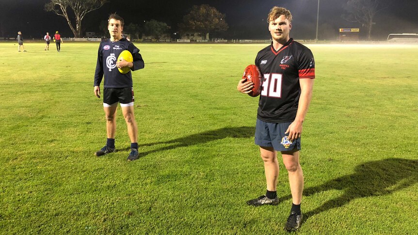 Two men stand apart from each other holding footballs