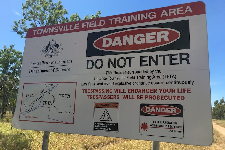 A sign in front of a rural military training ground warning against trespassing.