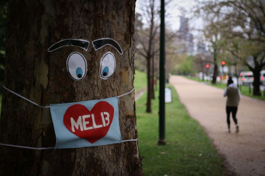 A picture of a person on a walking track going past a tree with eyes and eyebrows stuck on, with a Melb loveheart sign.