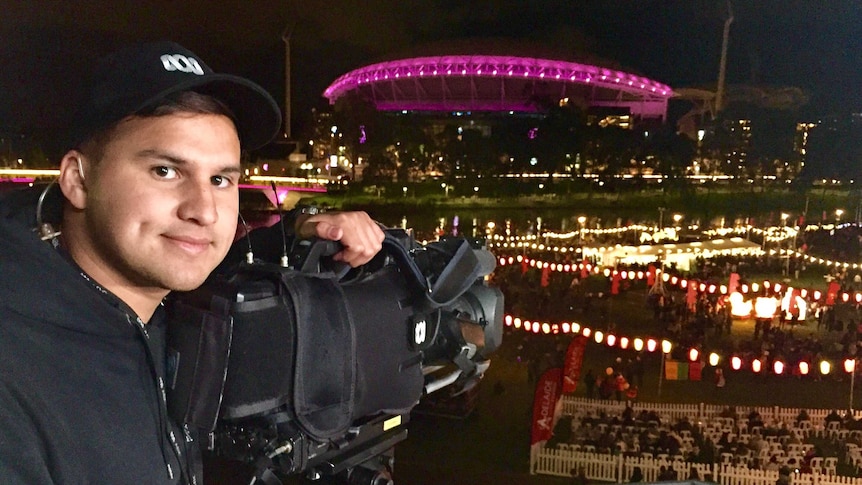 Night shot of Haidarr smiling while leaning on camera pointed at stadium lit up by pink lights.
