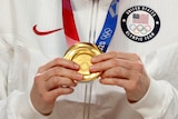 a close up on an athlete holding an Olympic gold medal while wearing their USA tracksuit