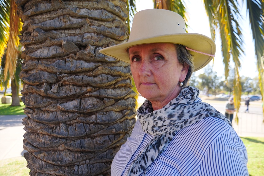 A woman with a striped shirt and wide brimmed hat standing outside.