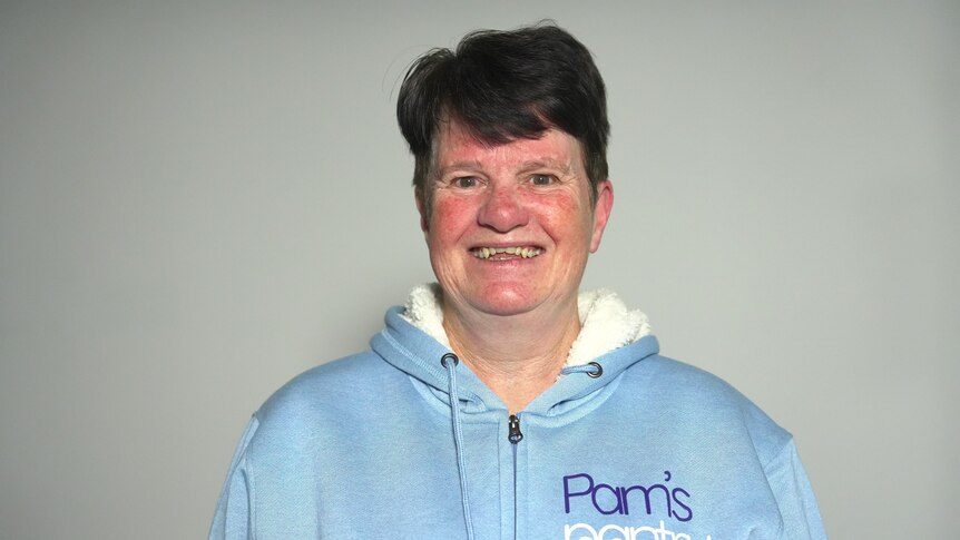Woman with short brown hair and a blue 'pam's pantry' jumper smiling