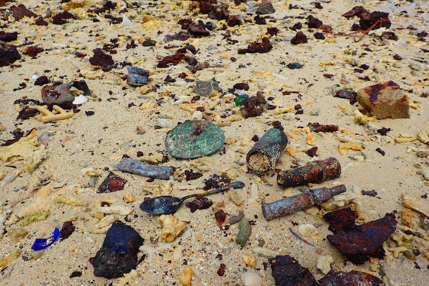 Bottles and metal lay in the sand on a beach.