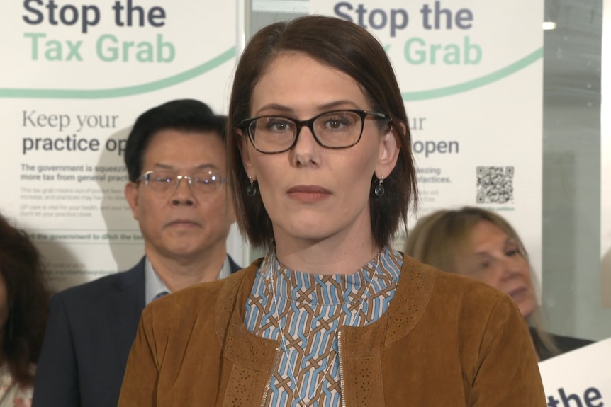 Anita Munoz wears black rimmed glasses, a brown jacket and brown and blue patterned shirt and stands with several people.