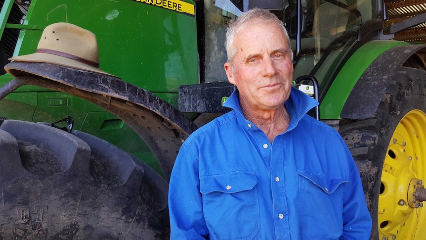 George Mills stands in front of a green tractor