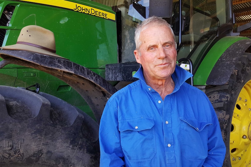 George Mills stands in front of a green tractor