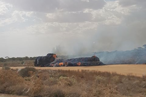 A hay truck on fire on an outback road.