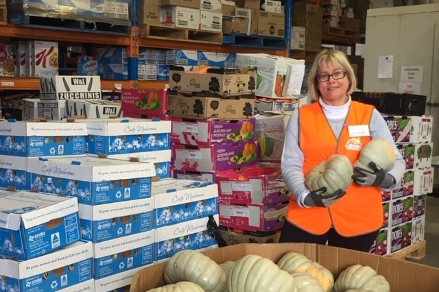 A woman stands in a food warehouse holding fruit.