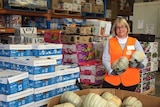 A woman stands in a food warehouse holding fruit.