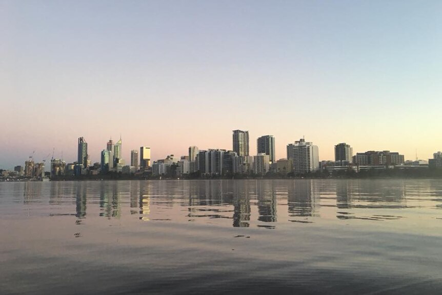 A clear sky over the Perth CBD skyline viewed from the Swan River with water in the foreground.