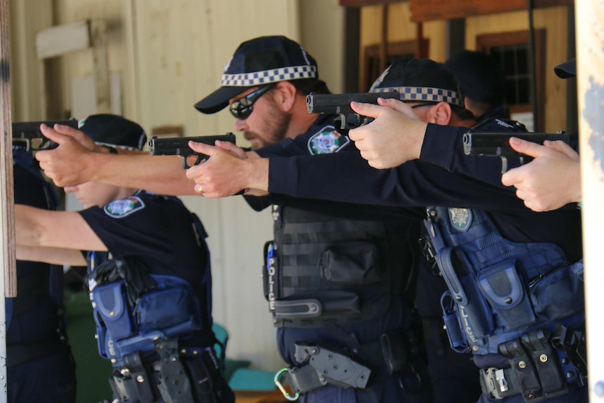 Queensland police officers stand in row with guns raised during pistol training.