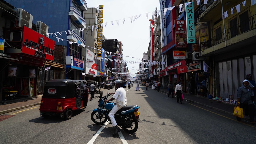 A man in white on a motorbike on a road with white mourning flags criss-crossed above the street.