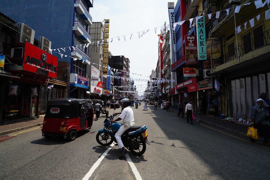 A man in white on a motorbike on a road with white mourning flags criss-crossed above the street.