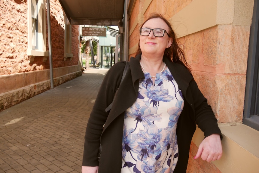 A woman stands in an alley and smiles off in the distance