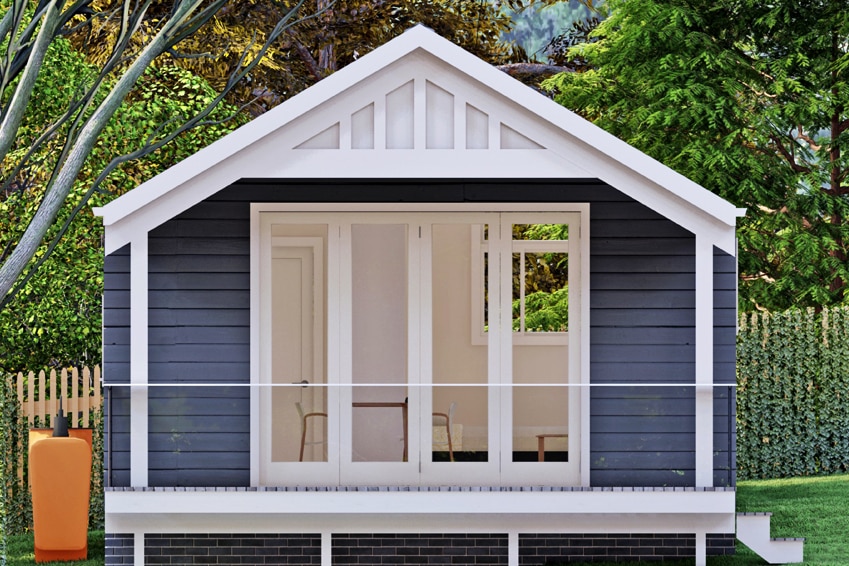 A small blue and white home sit in a green backyard. it has open white french doors.