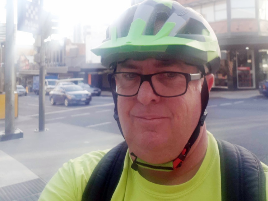 A man with a bicycle helmet on takes a selfie on a city street.