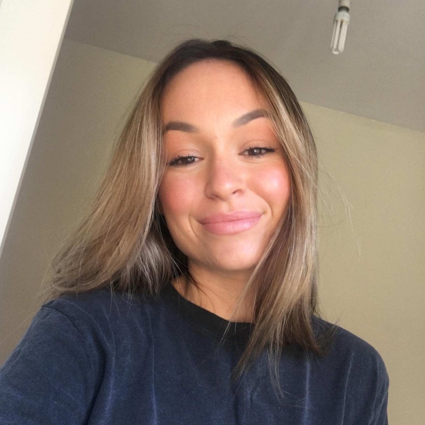 A young woman in a dark T-shirt smiles for a selfie