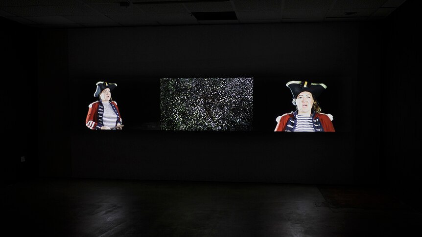 dark gallery with images on screen of people dressed in Captain Cook style clothing
