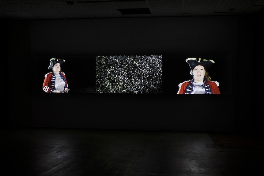 dark gallery with images on screen of people dressed in Captain Cook style clothing