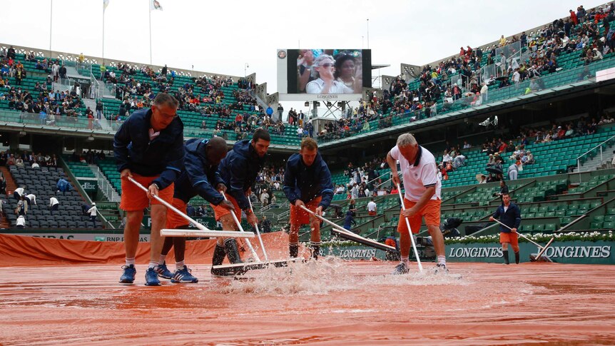 Court workers sweep away rain water from the court