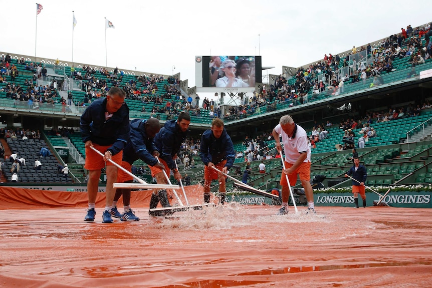 Court workers sweep away rain water from the court