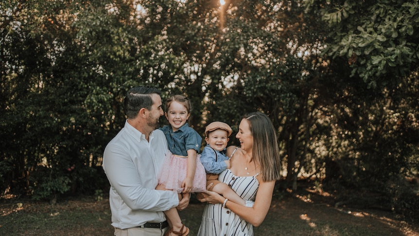 Young parents smile while holding their two young children.