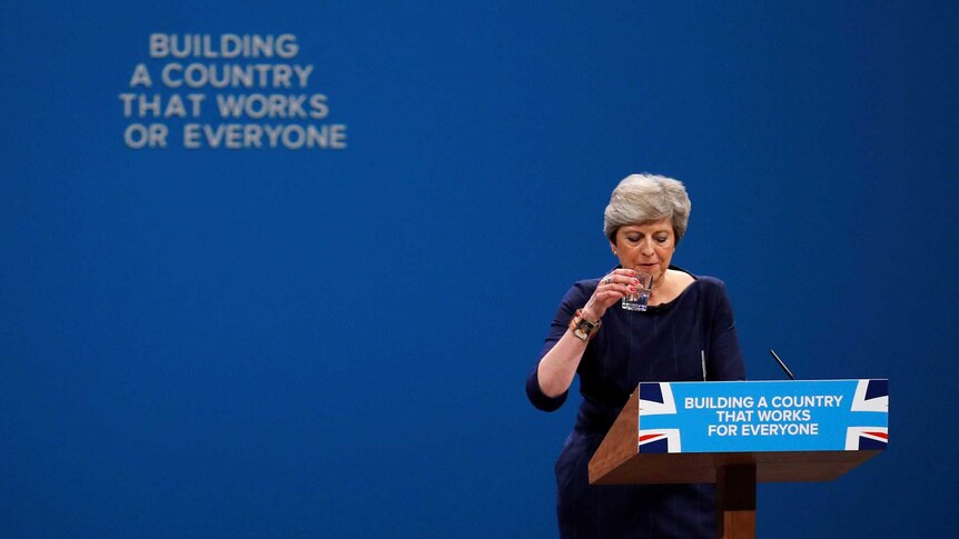 Theresa May stands in front of a slogan that is changed after a letter fell away