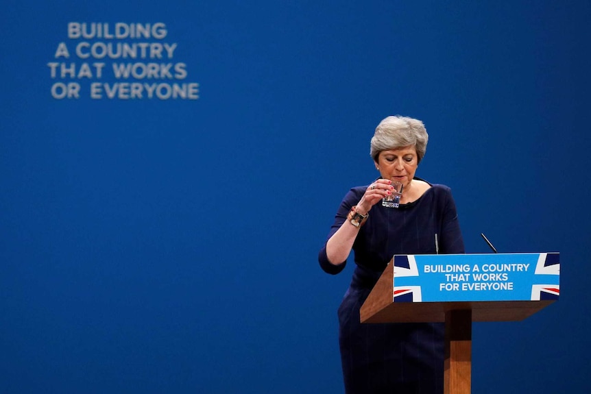 Theresa May stands in front of a slogan that is changed after a letter fell away