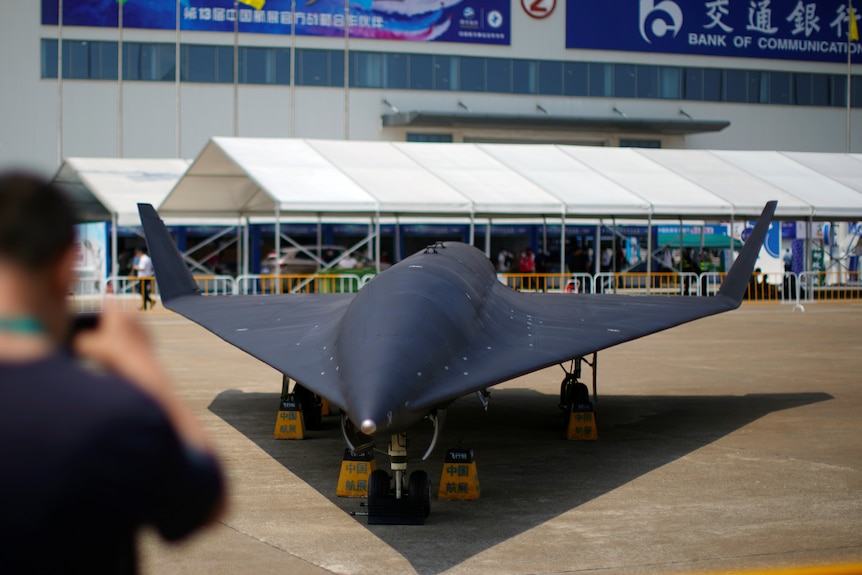 A person takes a photo of a black drone on a tarmac.