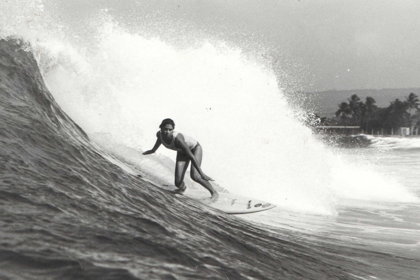 A black and white photo of a woman surfing a large wave.