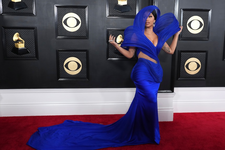 Cardi B wearing a bright blue fitted gown with a train and structured hood and sleeves that stand upright on their own. 