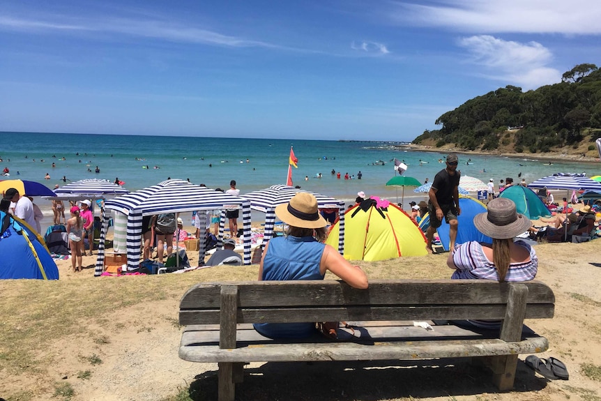 Two women sitting on a bench looking out at people on Lorne beach.