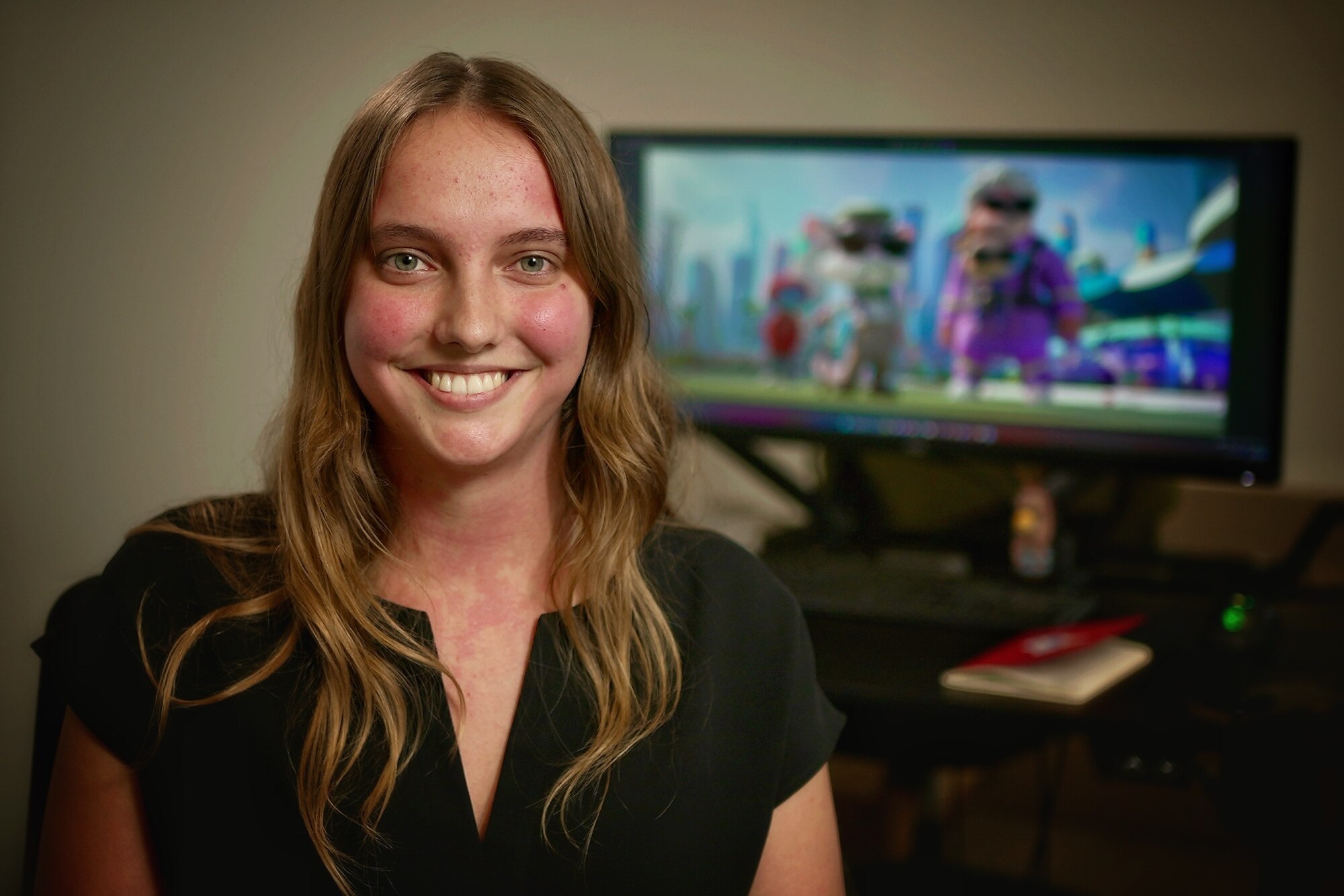 Anna smiles while sitting near a screen showing an animated film.