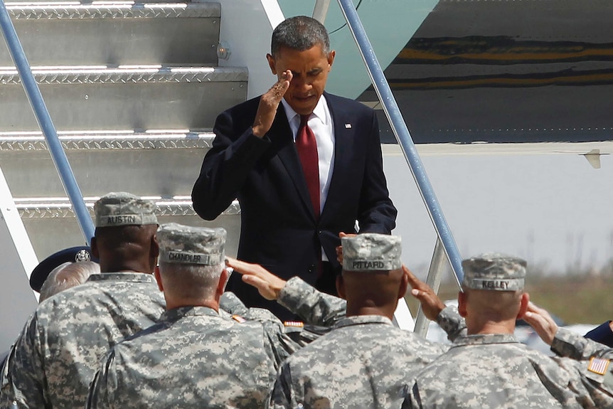 Former US president Barack Obama stands on plane stairs saluting a group of army personnel on the ground