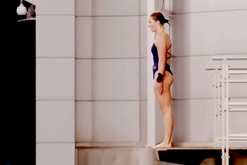 A still image of a video shows Nikita standing back up on a platform, poised, arms straight by her side